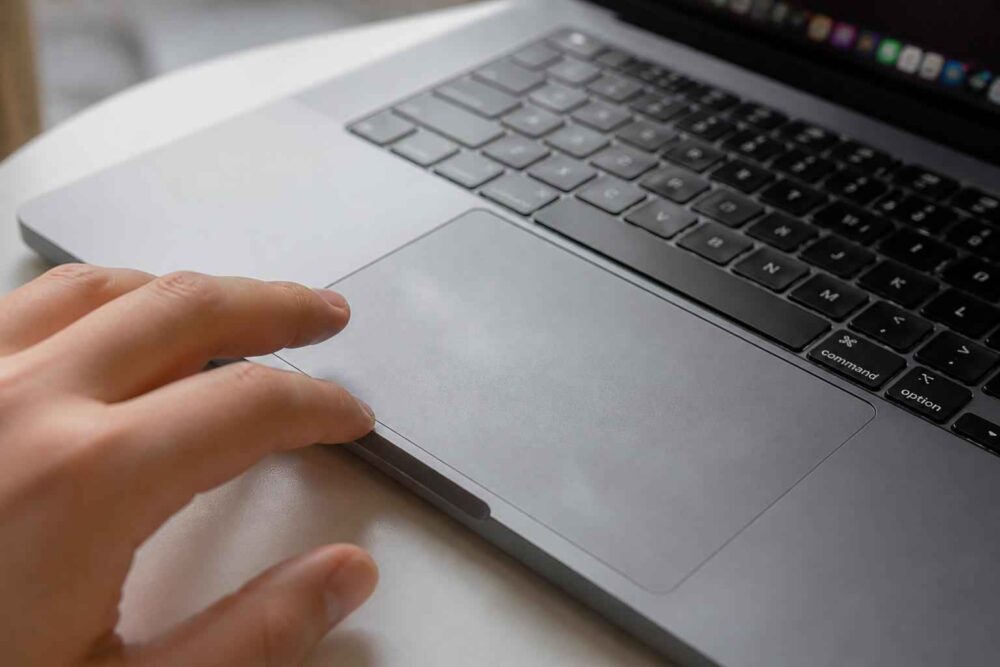 Dłoń obsługująca gładzik laptopa z widoczną klawiaturąაშორის
