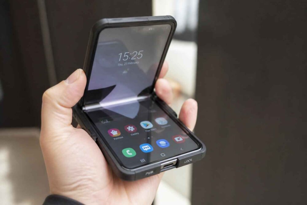 Otwarty składany smartfon trzymany w dłoni, z widocznym ekranem głównym i godziną 15:25