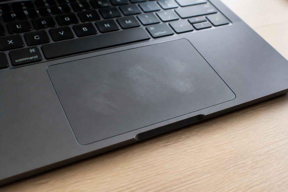 Touchpad laptopa na drewnianym biurku Zbliżenie na touchpad laptopa i fragment klawiatury na drewnianej powierzchni