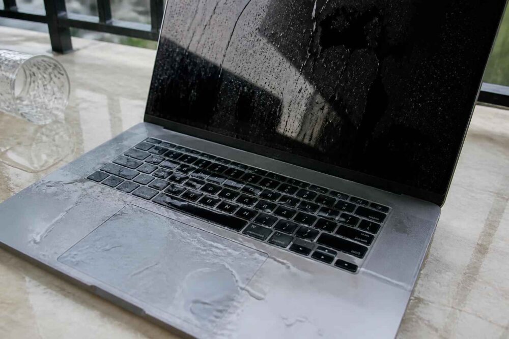 Laptop z mokrą klawiaturą i wodą na obudowie stojący na stole