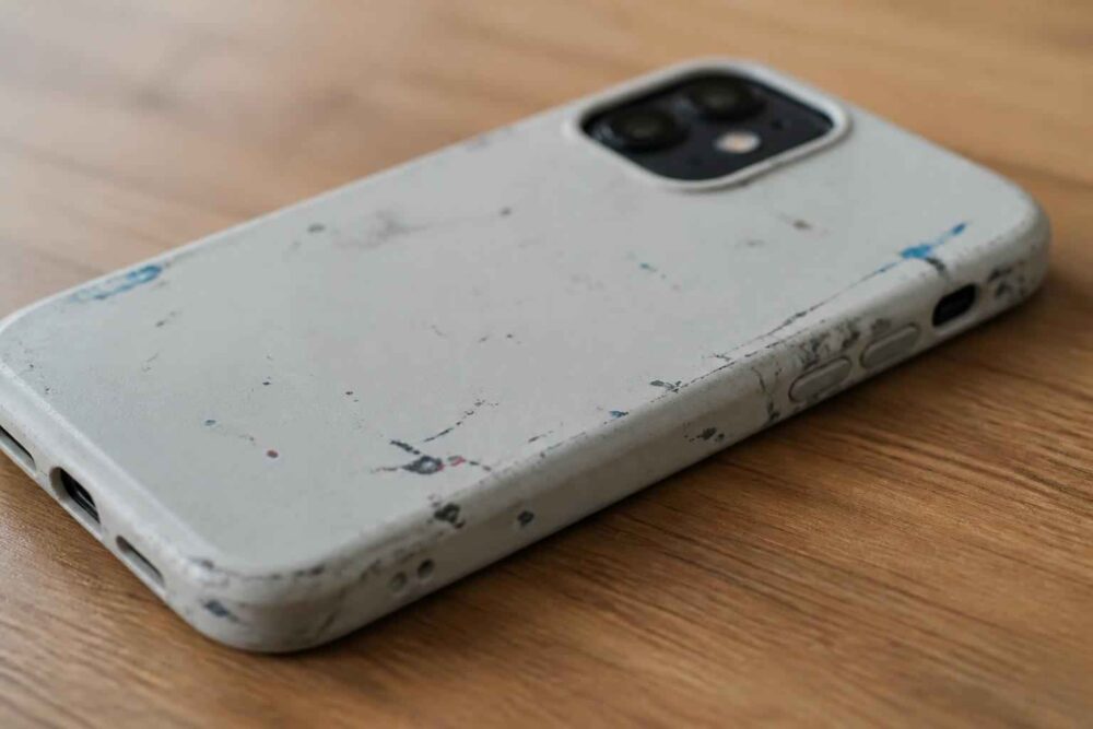 Biały telefon w mocno porysowanym etui leży na drewnianej powierzchniાન્ય